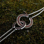 "Inseparable L" necklace featuring intertwined walnut and silver circles on a backdrop of textured moss.