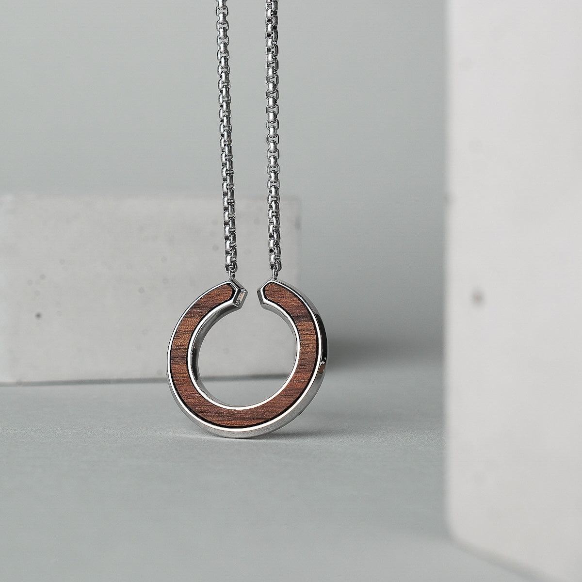 "Inseparable L", a walnut and silver necklace, featuring a sleek circular pendant design.