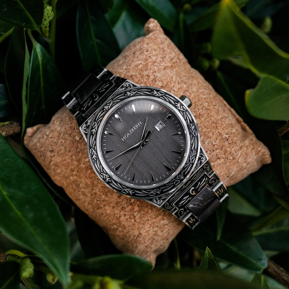 "Misir" watch featuring intricate detailing and a sophisticated maple style on a cushion surrounded by greenery.