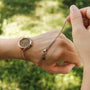 "Bracelet fastening tool", a bracelet fastening tool in rose gold, shown in use outdoors.