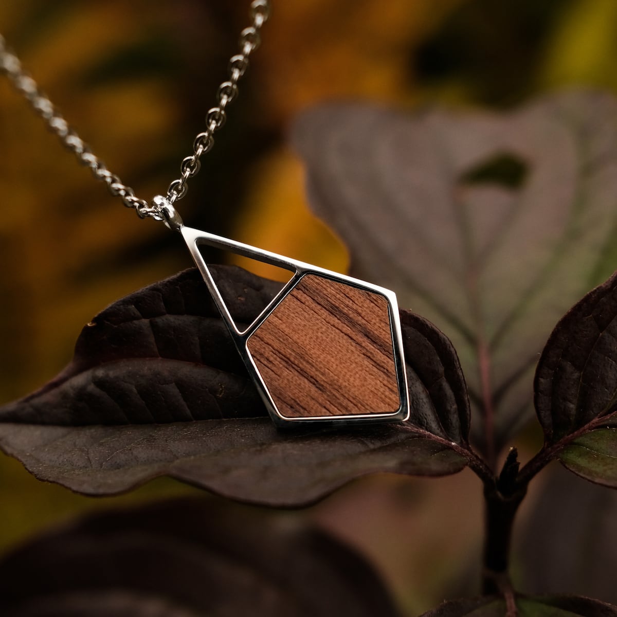 "Mandala Necklace" pendant necklace featuring geometric walnut and silver design, elegantly styled against a natural backdrop.