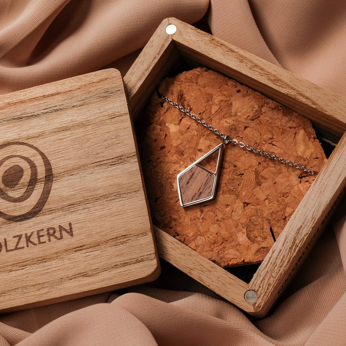 "Mandala Necklace" necklace features a geometric pendant with a walnut and silver design, displayed in a wooden box.