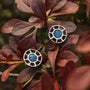 "Amulet Earrings", elegant earrings in marble and silver, featuring a circular design set against vibrant foliage.
